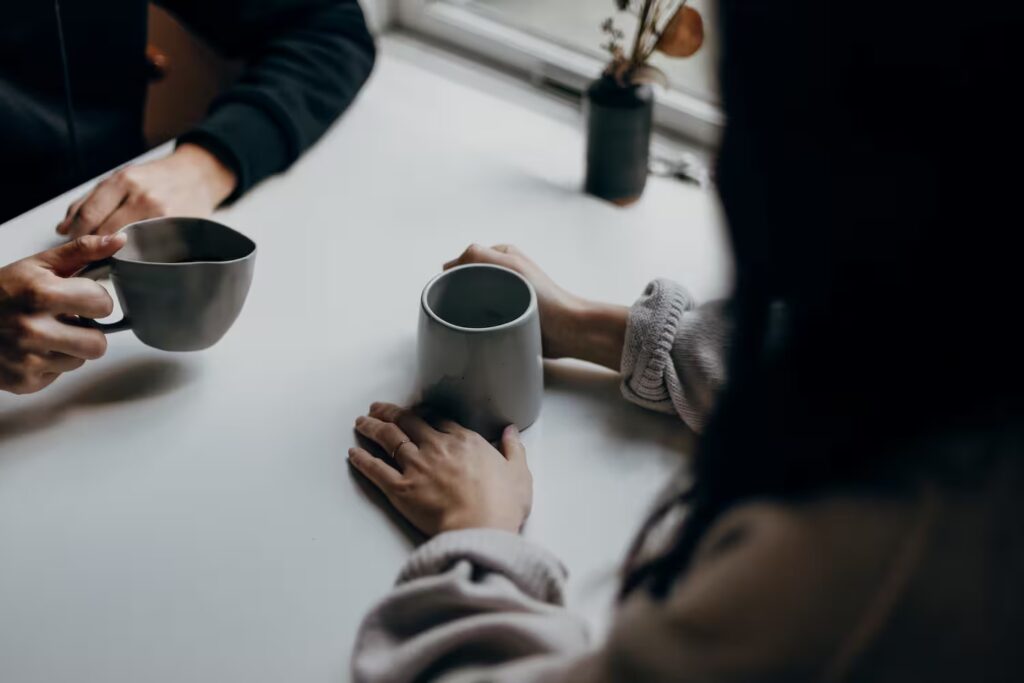 Two people have a difficult conversation about accountability while drinking coffee.